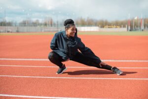 A woman in activewear stretches on a red running track outdoors, preparing for a workout.