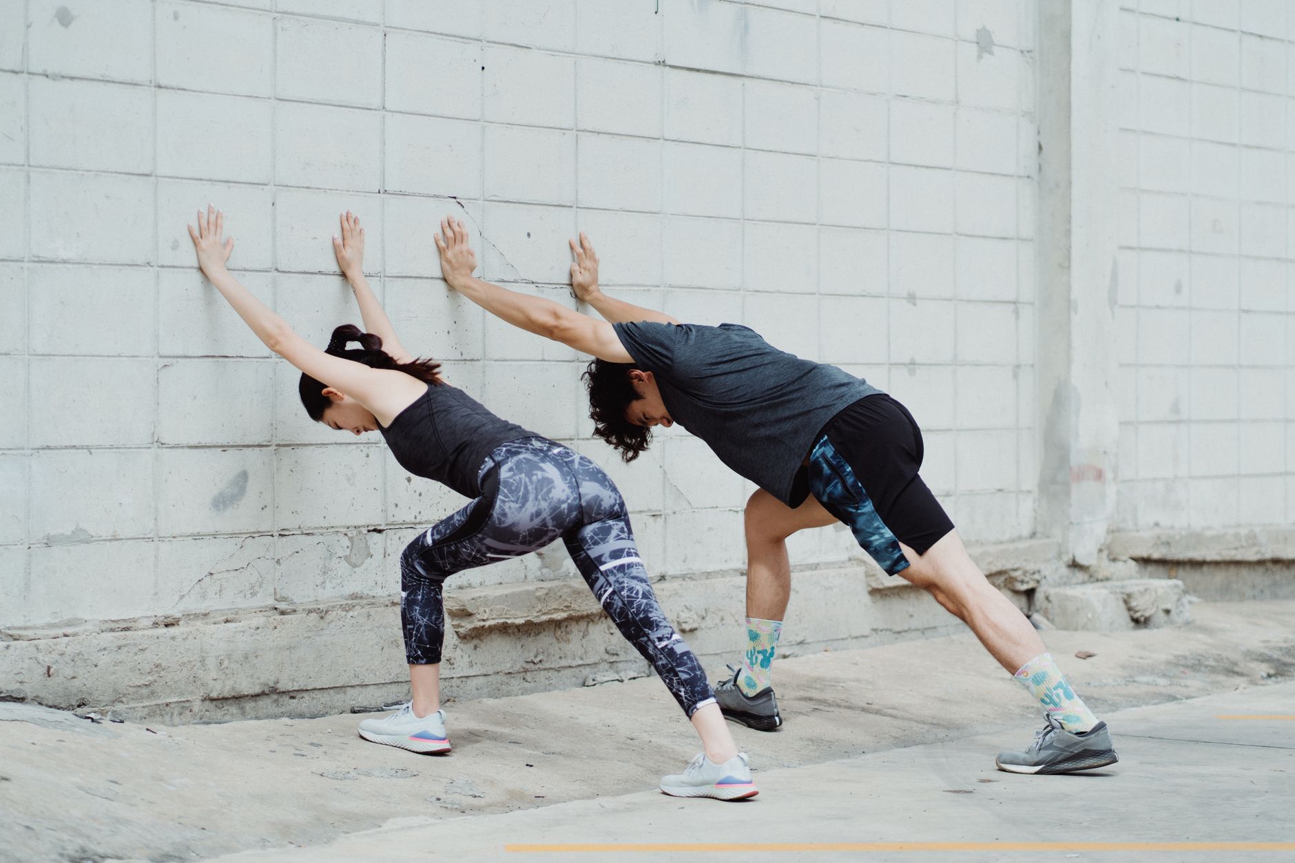 A couple stretches together outdoors on a concrete surface, emphasizing fitness and urban exercise.