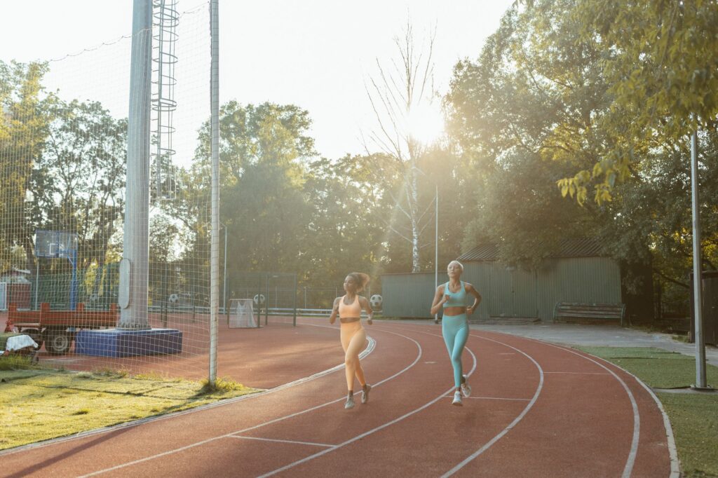 Two women jogging on an outdoor track, enjoying exercise and fitness in the morning sun.