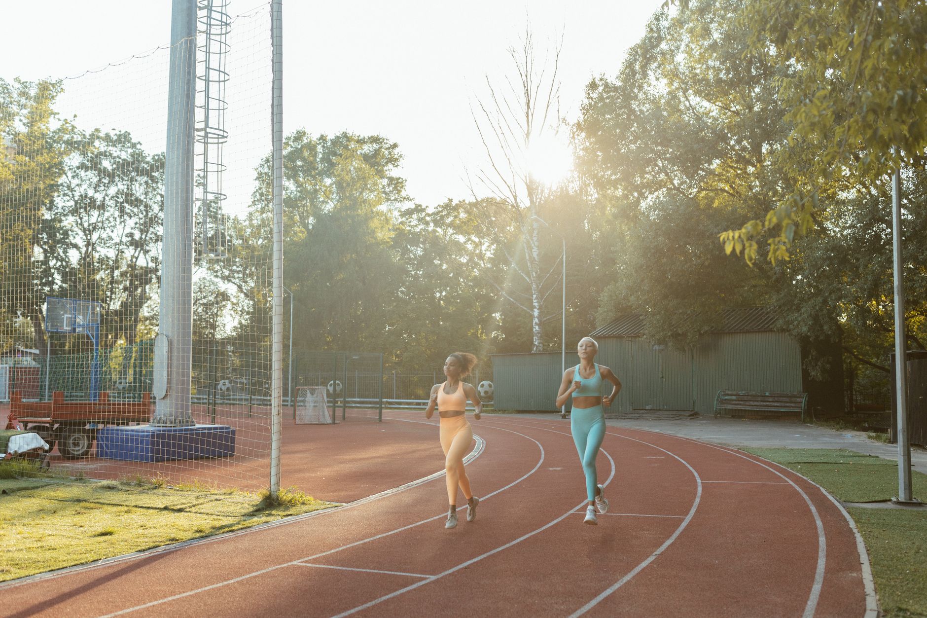 Two women jogging on an outdoor track, enjoying exercise and fitness in the morning sun.