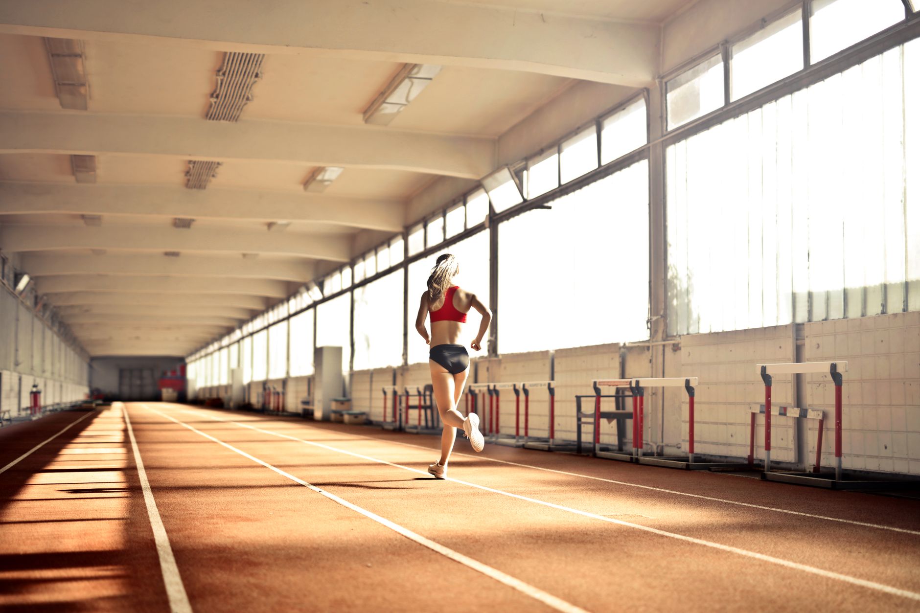 Woman in athletic wear running on an indoor track, showcasing speed and determination.